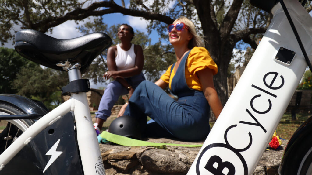 two happy ladies sitting next to a bike share bicycle.